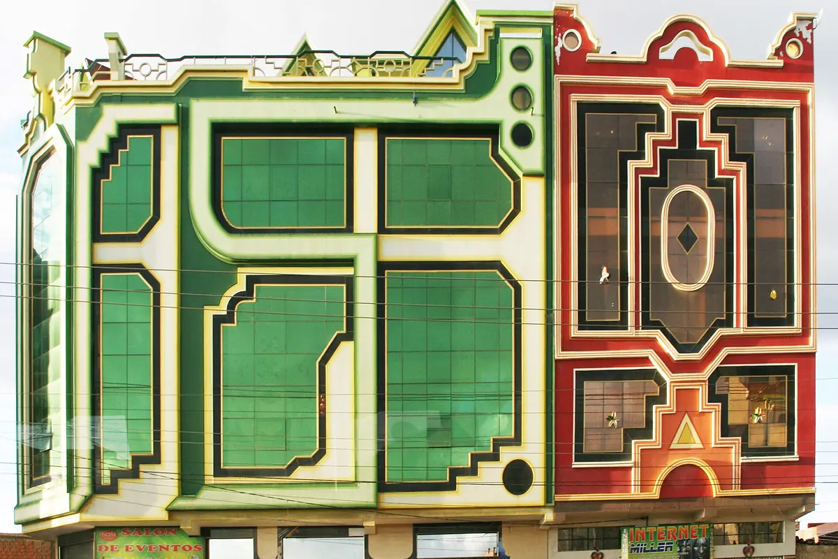 Two tall buildings side by side in El Alto, one with a green and cream facade of angular windows and one in red with a stepped geometric pattern